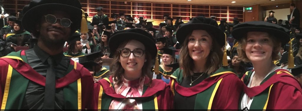 Photgraph of four smiling MRC LID students at the St George's graduation ceremony in the Barbican on 24 July 2024. They are wearing SGUL doctoral robes. From left to right: Nathan Simpson, Emily Woodock, Claire Broad, and Sally Hayward.